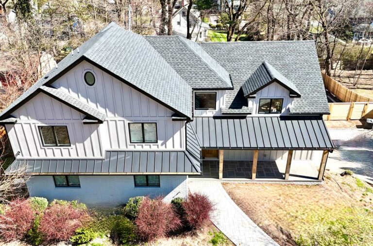 aerial-view-of-dark-gray-roof-and-house-with-white-siding-and-green-and-red-shrubs-in-front-yard