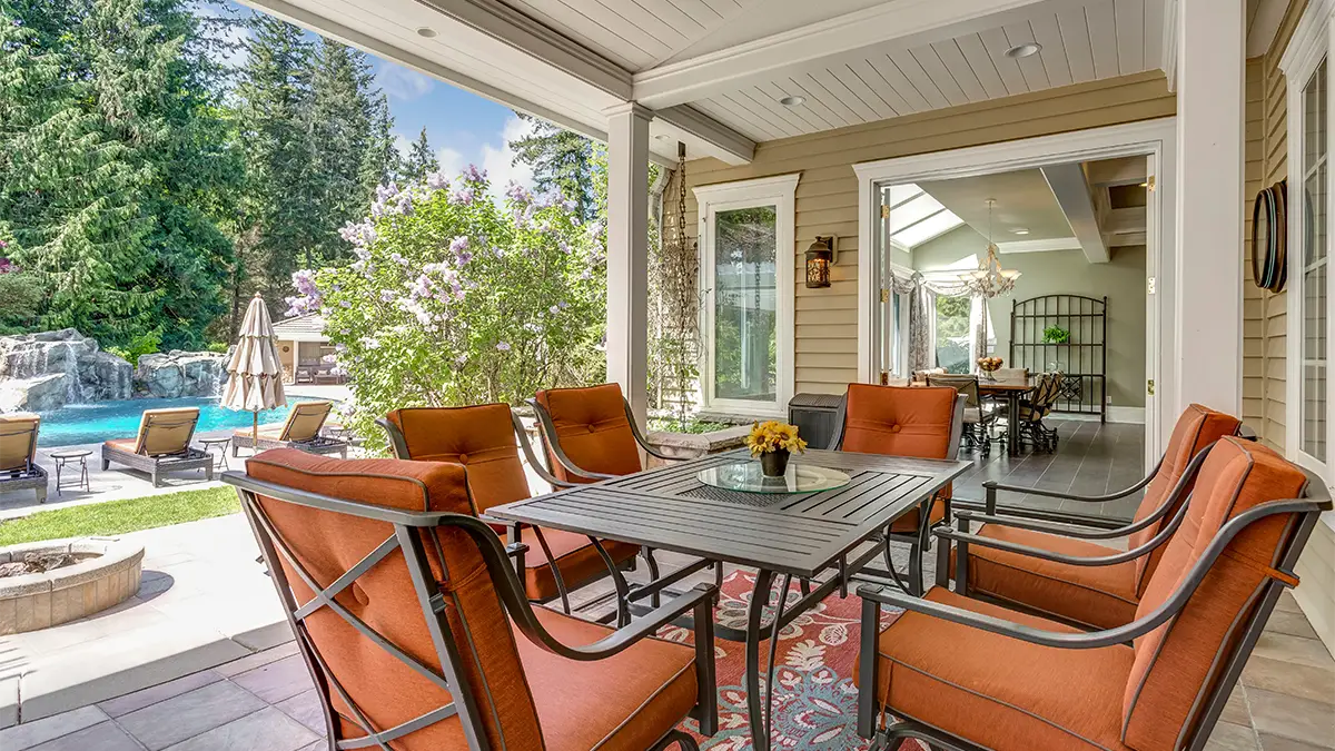 An open back porch with a dining set overlooking a backyard with a pool.