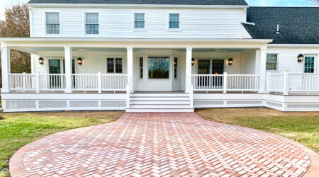 A back porch on a white house featuring paving stones leaving to large back stairs.