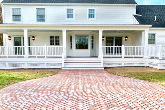 A back porch on a white house featuring paving stones leaving to large back stairs.