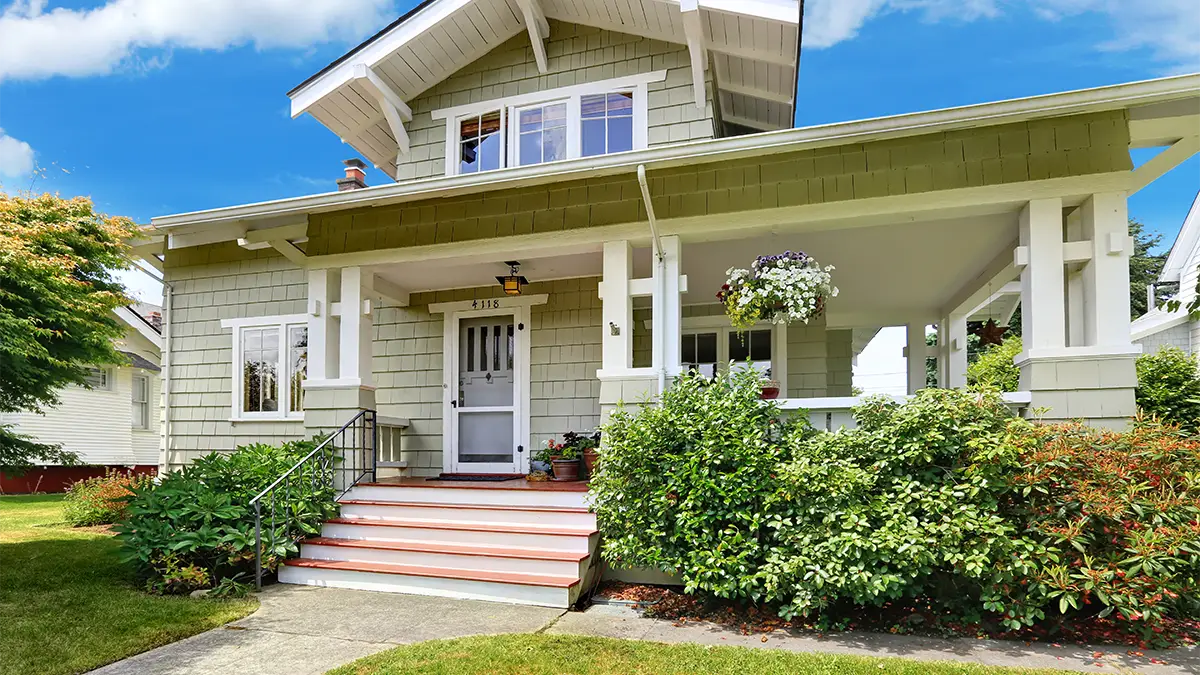 A front porch on a small craftsman style bungalow with landscaped shrubs.