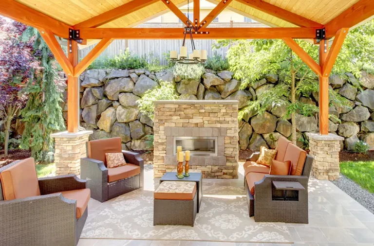 An open pavillion featuring a stone fireplace, open wood beams, and ample outdoor seating.