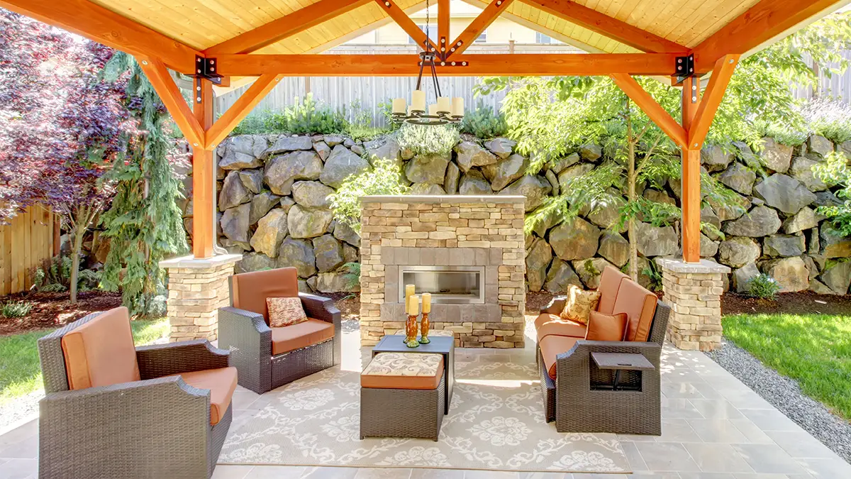 An open pavillion featuring a stone fireplace, open wood beams, and ample outdoor seating.