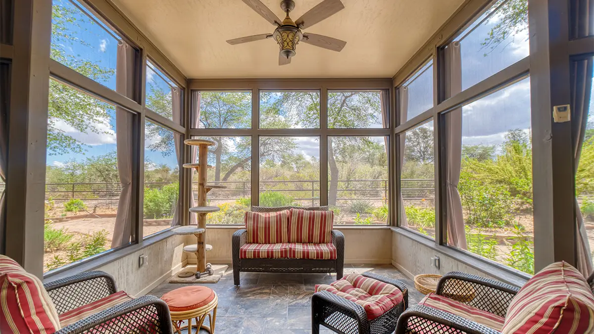 A furnished screened sunroom featuring ample seating arraingments, tall screened windows, a ceiling fan, and a cat tree in the corner.