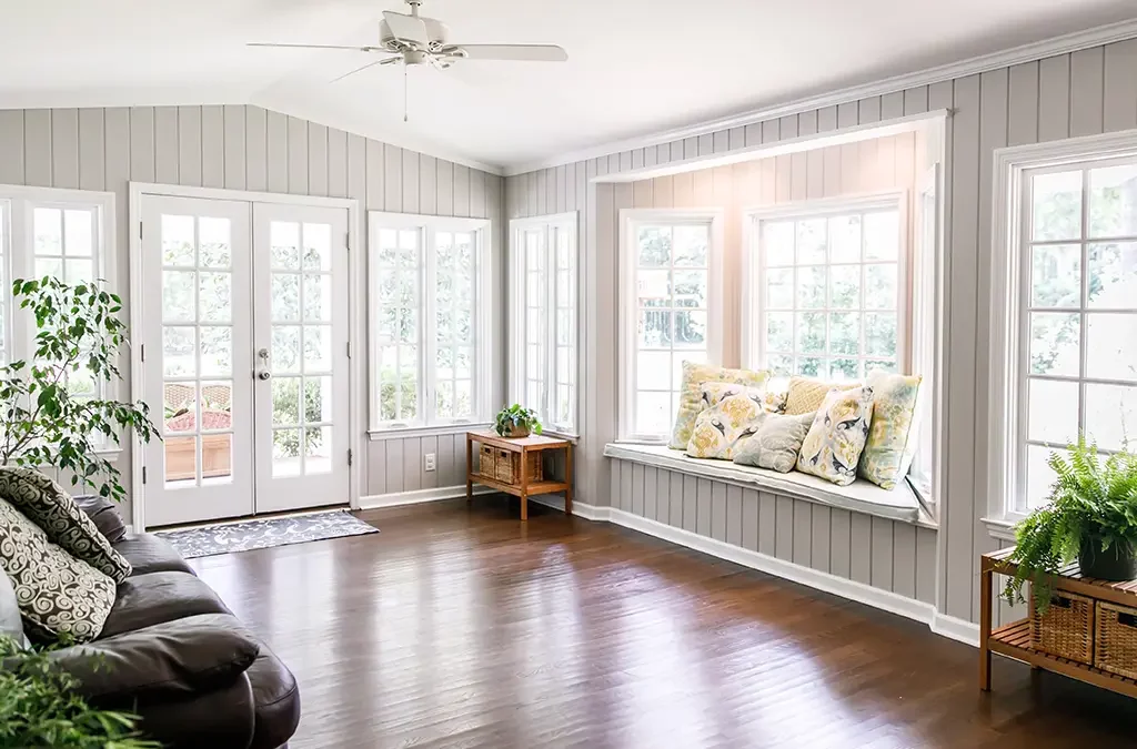 A sunroom with hardwood flooring, installed windows and doors, a wall-seating area, and ceiling fan.