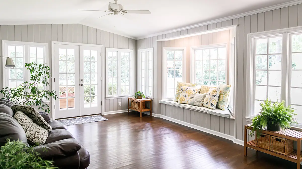 A sunroom with hardwood flooring, installed windows and doors, a wall-seating area, and ceiling fan.