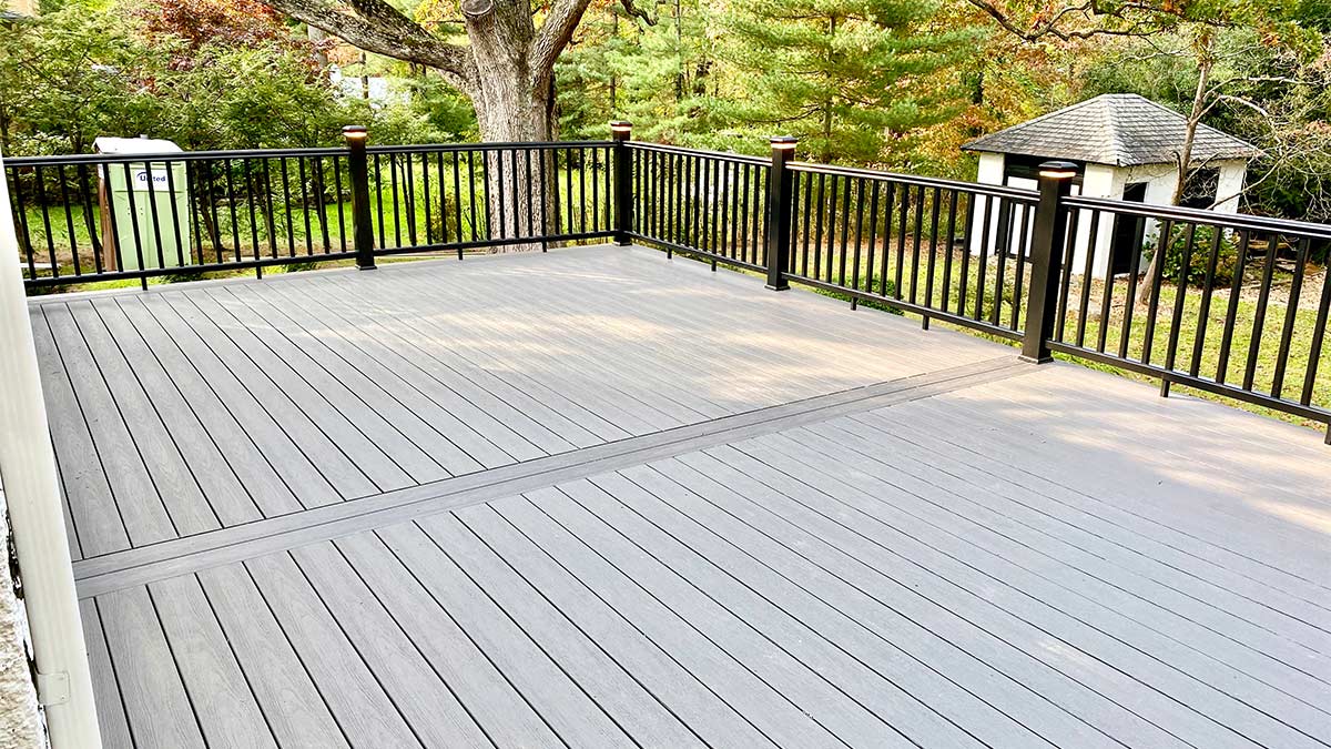 A deck with Azek boards of a medium brownish-grey and black railing overlooking a backyard in New Jersey.