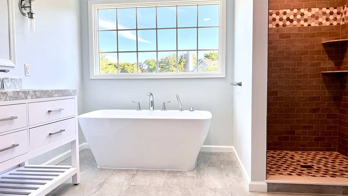 A bathroom with new tile, vanity, and freestanding tub. To the left is a built-in shower that has bronze accent tiles.