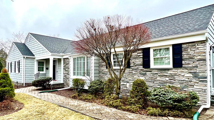 blue-and-stone-ranch-home-with-black-shutters-and-tree-with-landscaping