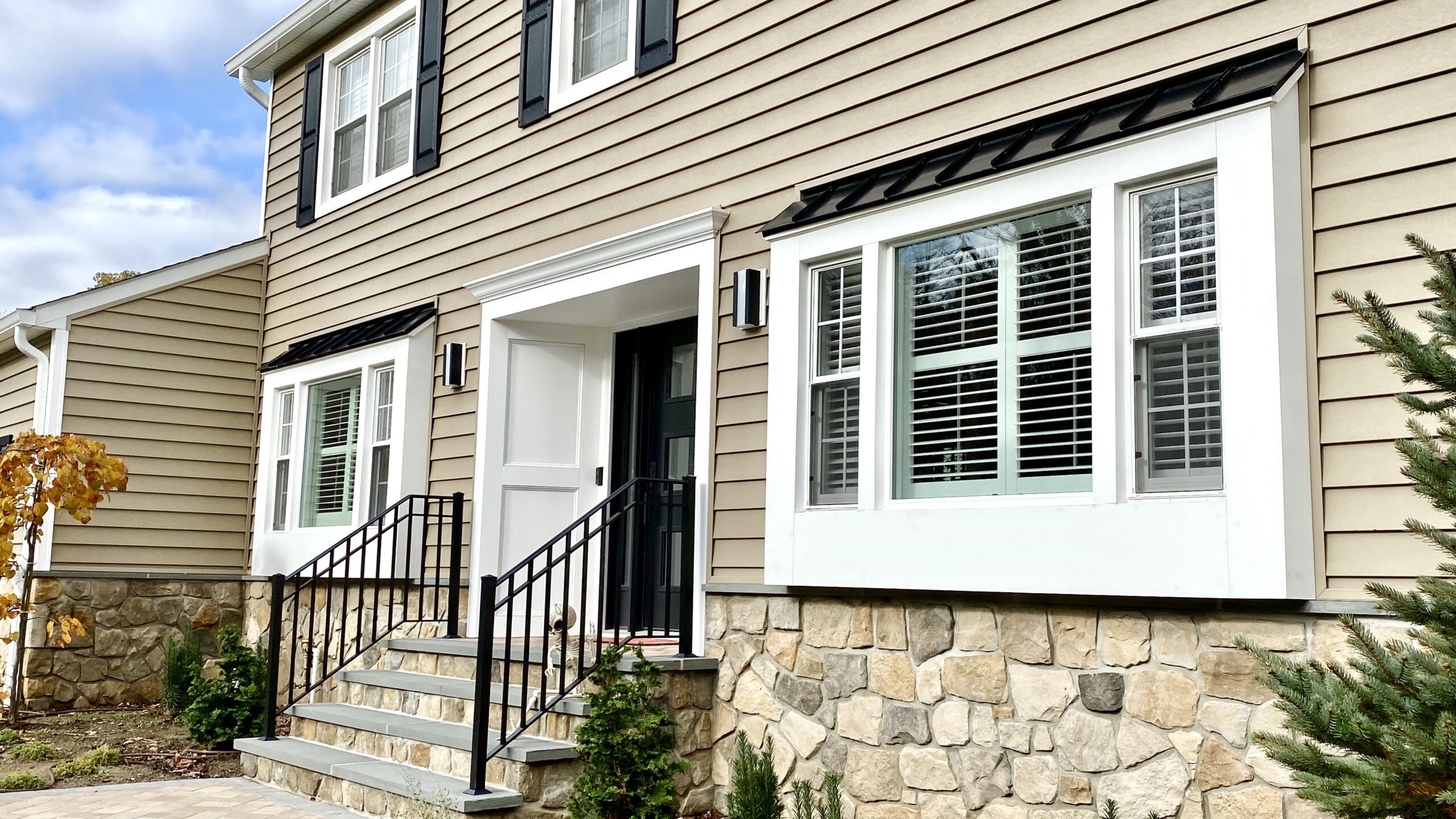 Two-story home with beige siding, stone foundation, and black-trimmed windows.