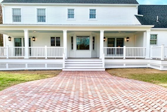 A back porch on a white house featuring paving stones leaving to large back stairs.