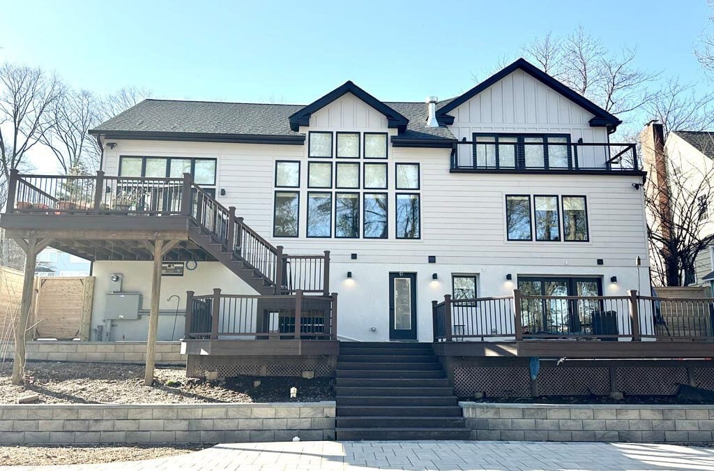 Rear exterior of a modern farmhouse-style home with white board-and-batten siding, black trim, large windows, and a multi-level deck with dark wood railings.