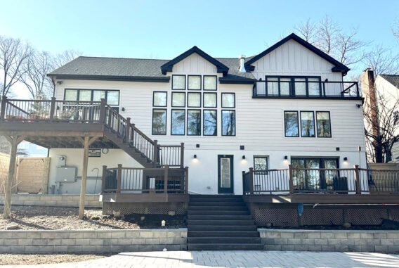 Rear exterior of a modern farmhouse-style home with white board-and-batten siding, black trim, large windows, and a multi-level deck with dark wood railings.